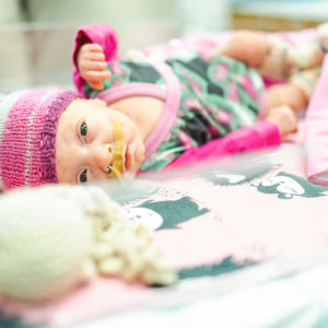 Vastasyntynyt vauva vaaleanpunaisessa pipossaan makailee patjan päällä letku nenässään ja laastari huulen yläpuolella.