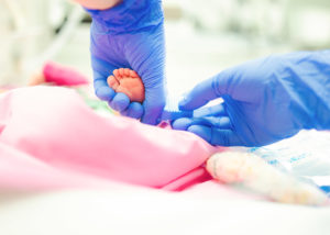 Kädet, joissa on siniset kumihanskat, ottavat näytettä vauvan jalasta.